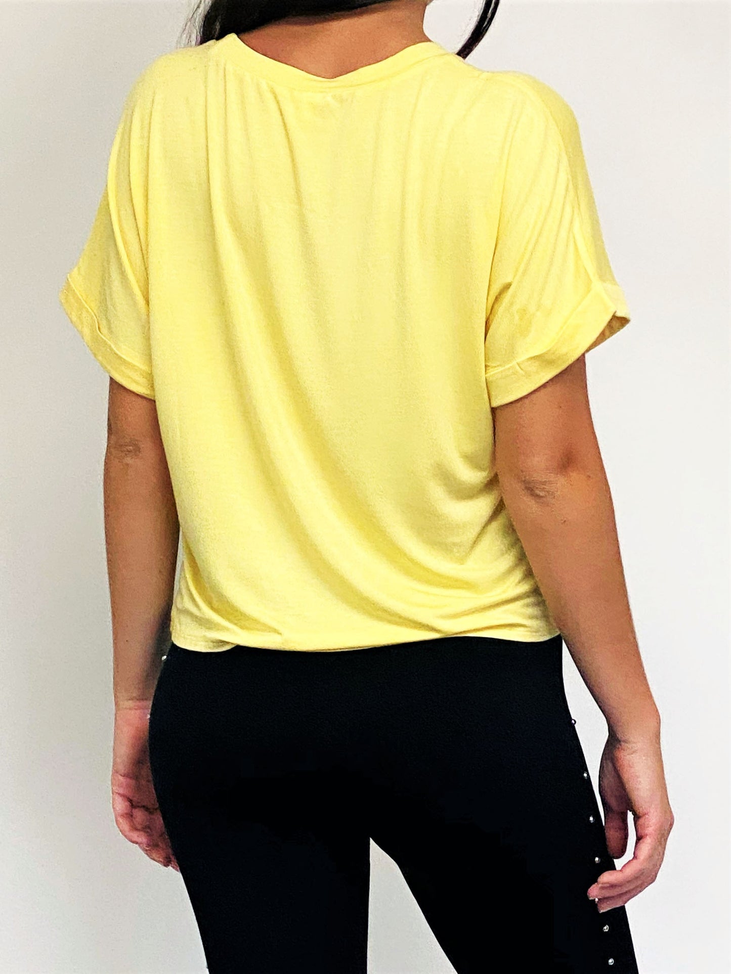 A woman wearing a bright yellow short-sleeve top and black pants, shown from the back against a plain light background.