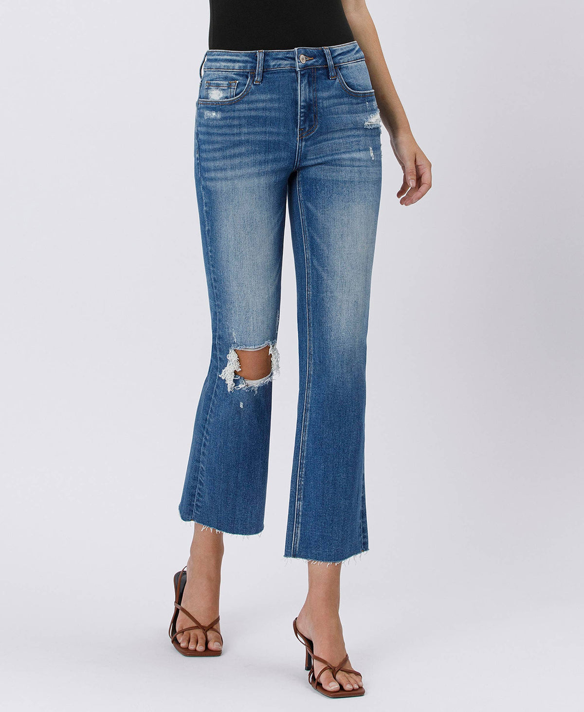 Blue jeans with distressed details worn by a person on a white background