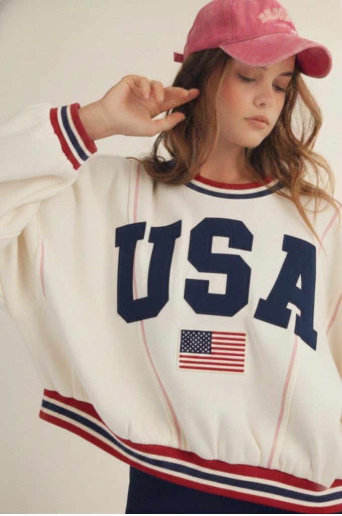 Person wearing a white sweatshirt with 'USA' and an American flag, paired with a pink cap.