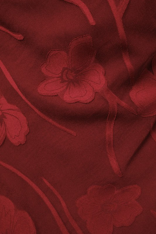A close-up of a deep red fabric with tonal floral embroidery and embroidered stems.