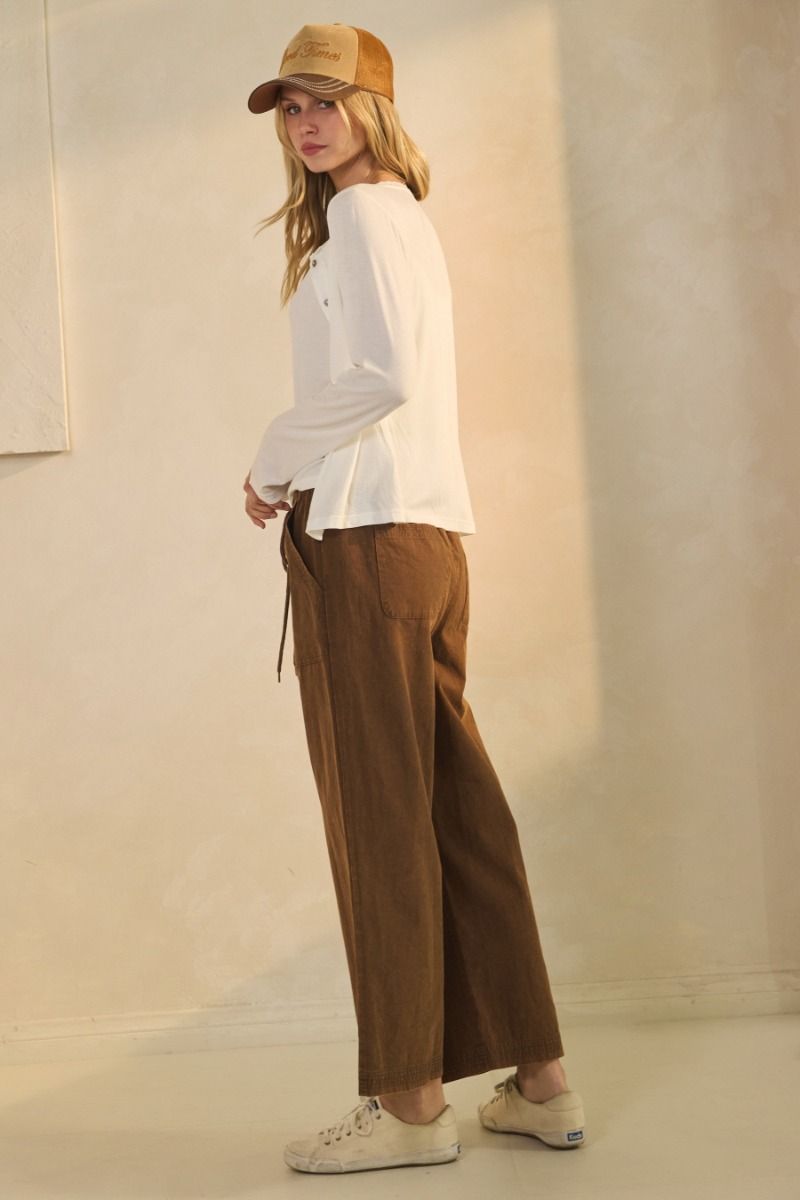 Woman wearing a white top, brown pants, and a beige cap against a plain background