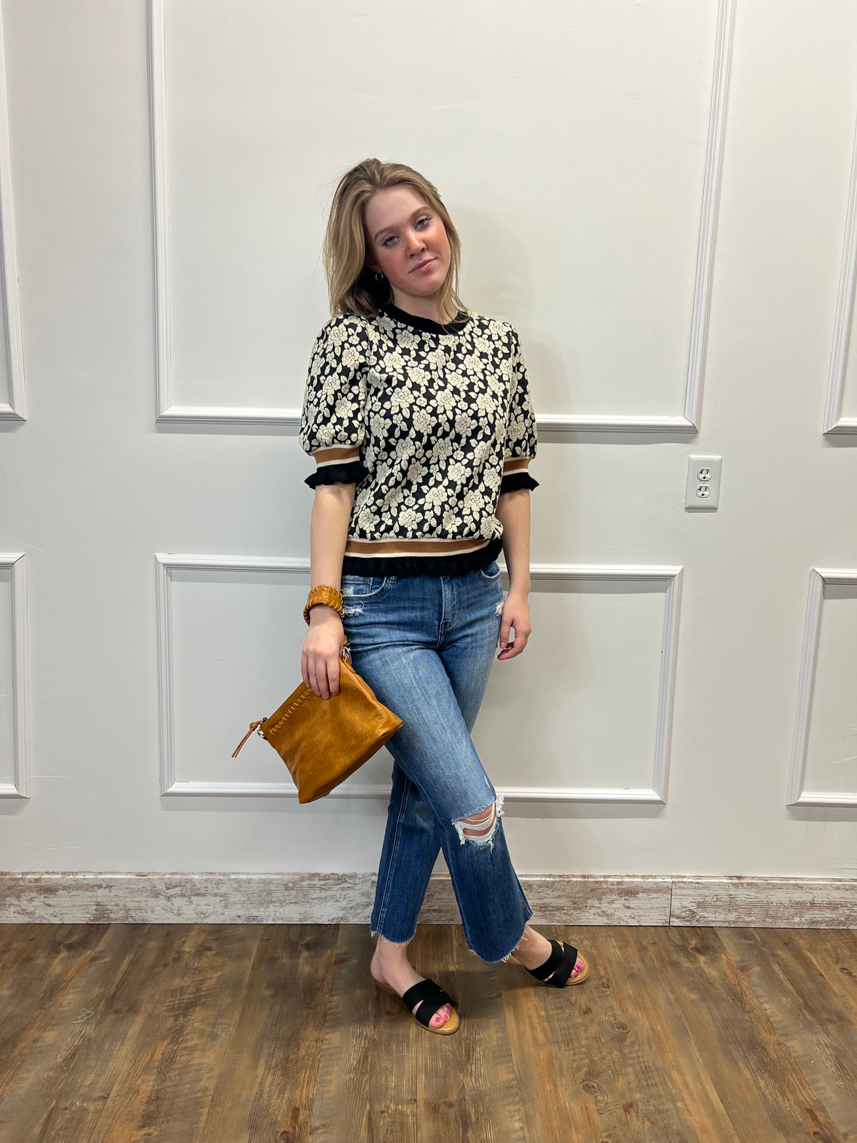 Woman standing in front of a white door holding a brown clutch.