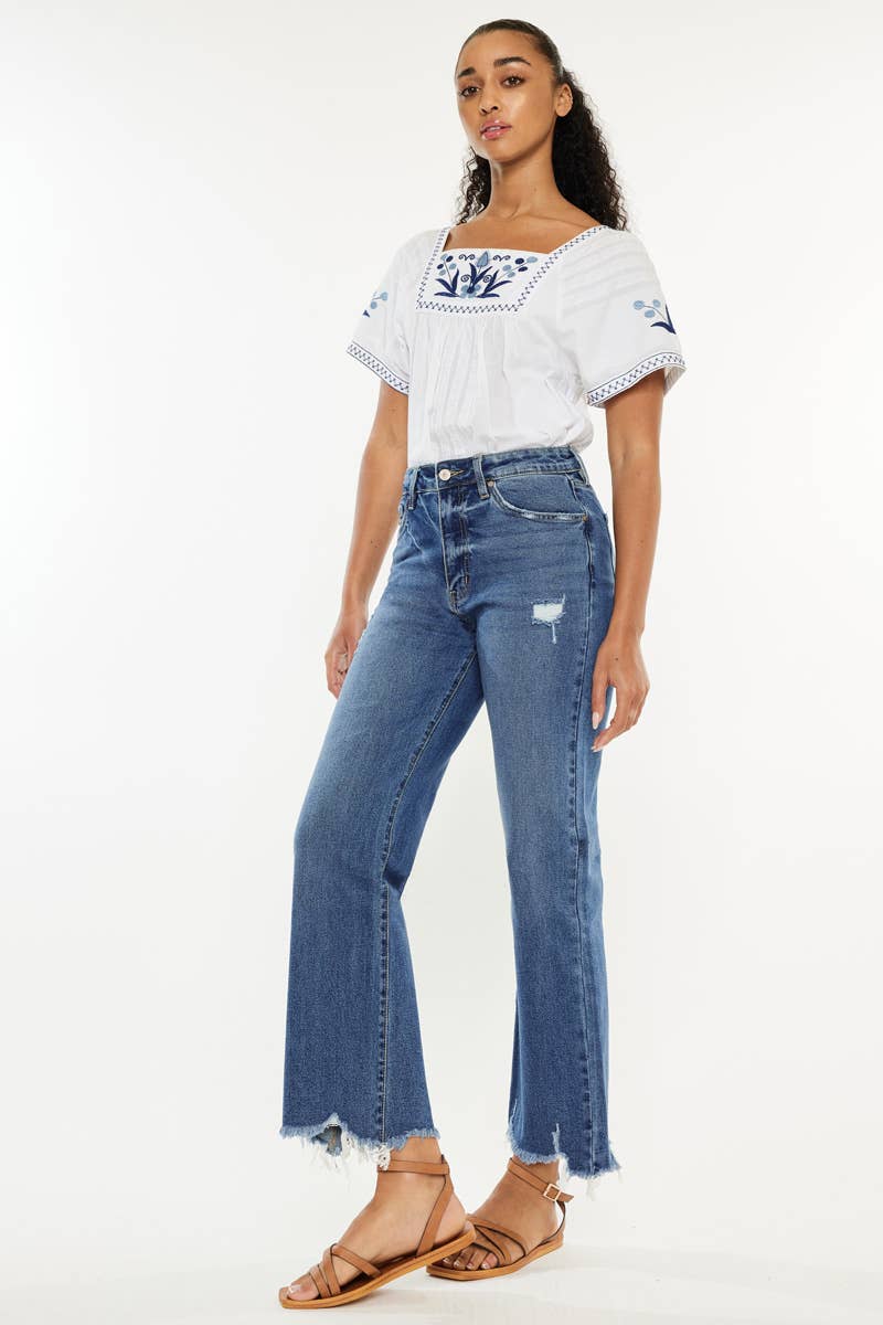 Woman wearing a white top with blue embroidery and blue jeans on a white background