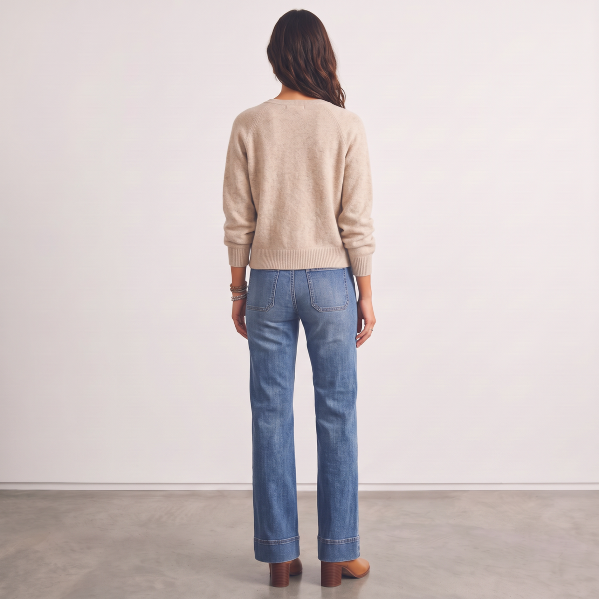 Back view of a woman wearing an Apricot Lane Duluth beige knit cardigan with blue jeans and brown heeled boots.
