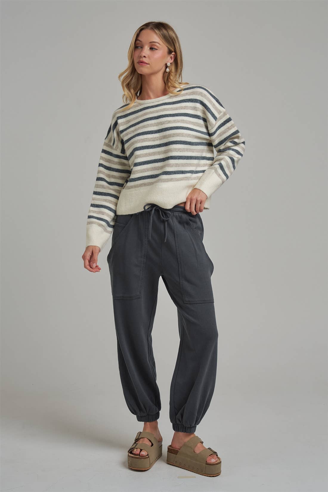 Model wearing Apricot Lane Duluth Dakota cargo joggers in charcoal with a striped sweater and platform sandals.
