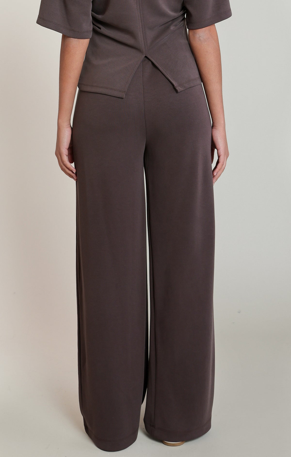 Person wearing a brown outfit with wide-leg pants on a plain background