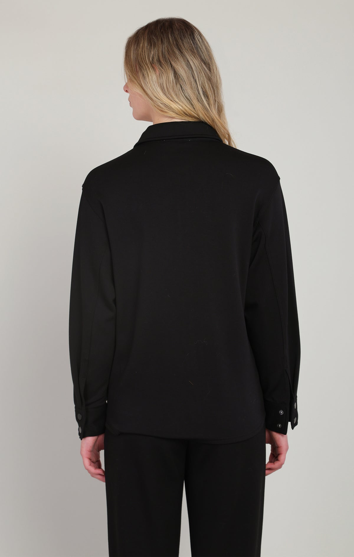 Person wearing a black jacket and pants on a plain background