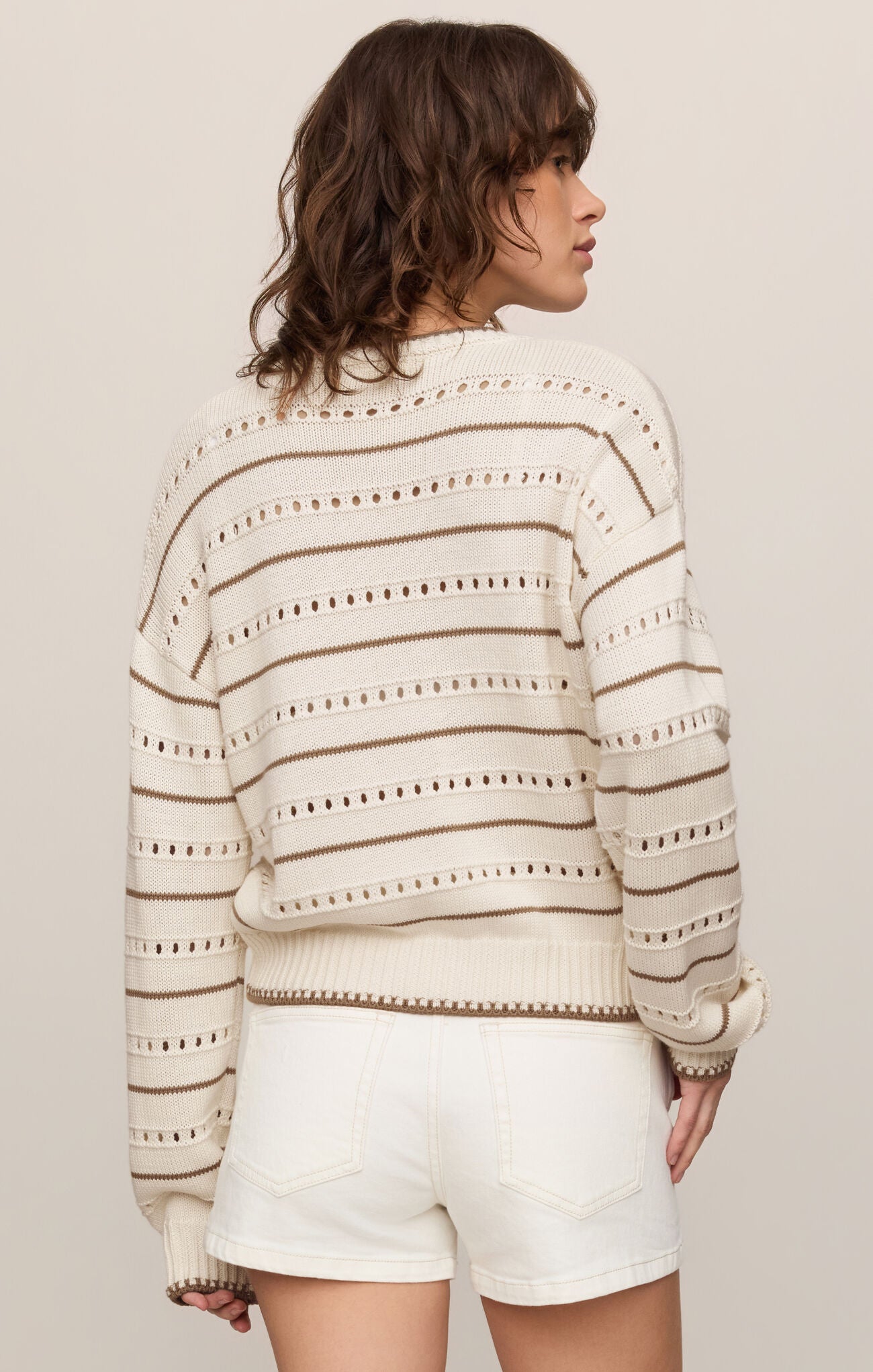 Woman wearing a striped sweater and white shorts against a plain background