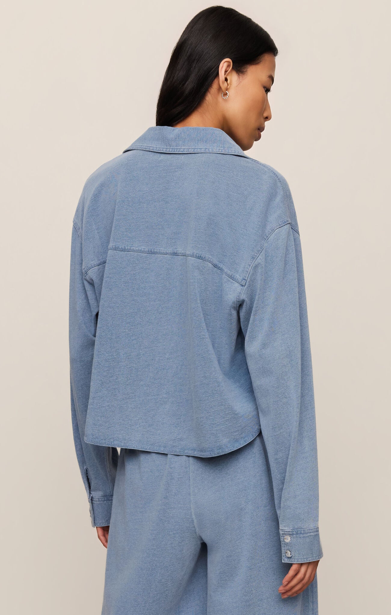 Person wearing a blue denim jacket and pants on a beige background
