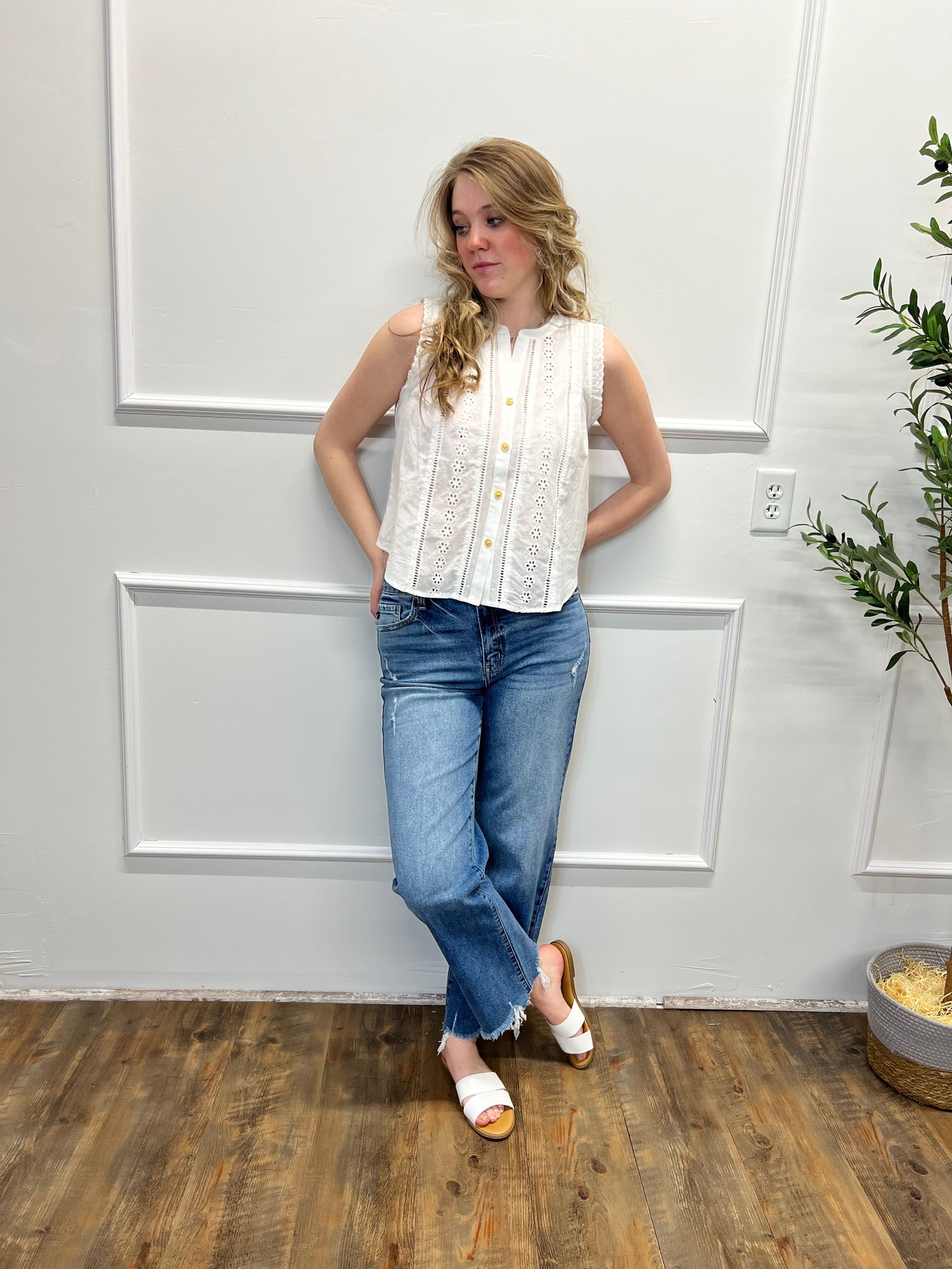 Girl in white top and jeans against white wall with plant