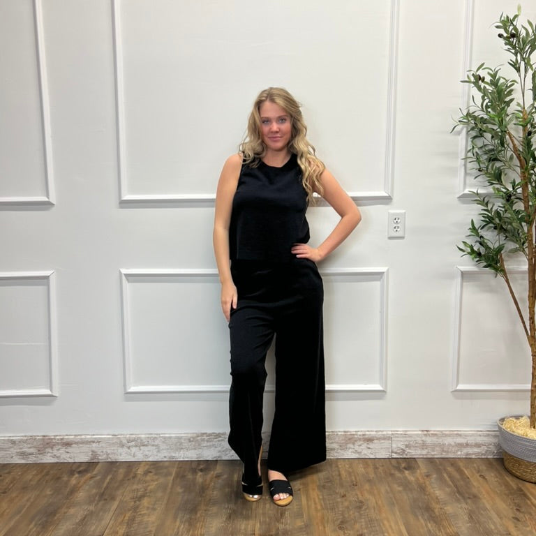 Woman in a black outfit standing in a room with white paneled walls and a plant.