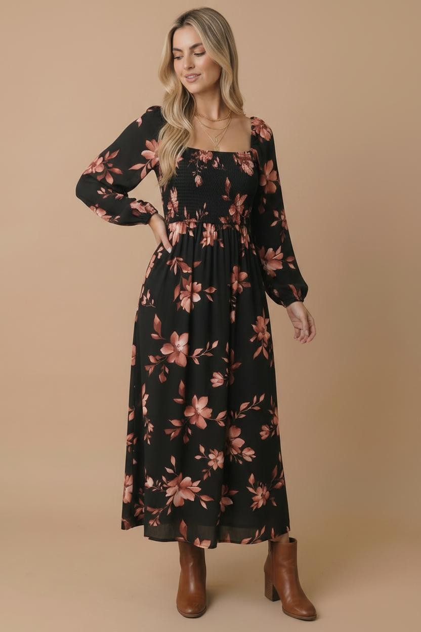 A woman modeling a long-sleeve black maxi dress with a dusty rose floral print, paired with brown ankle boots, against a solid beige studio background.