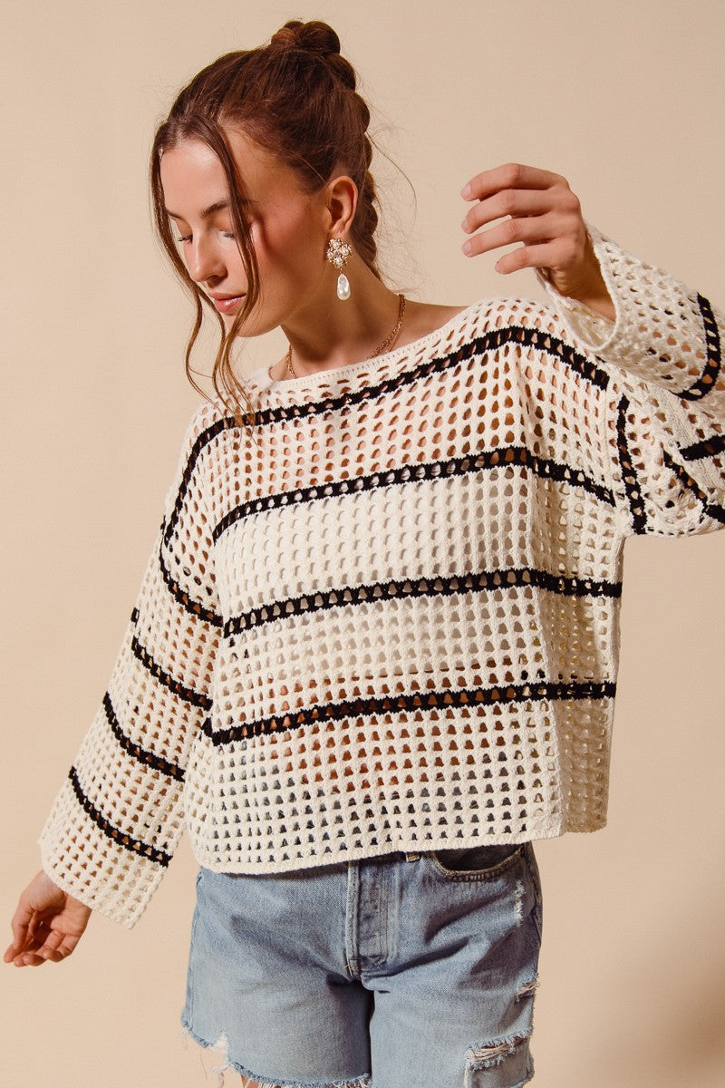 Woman wearing a white and black striped sweater with denim shorts on a beige background