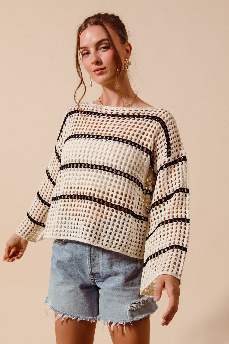 Woman wearing a black and white patterned sweater with denim shorts on a beige background