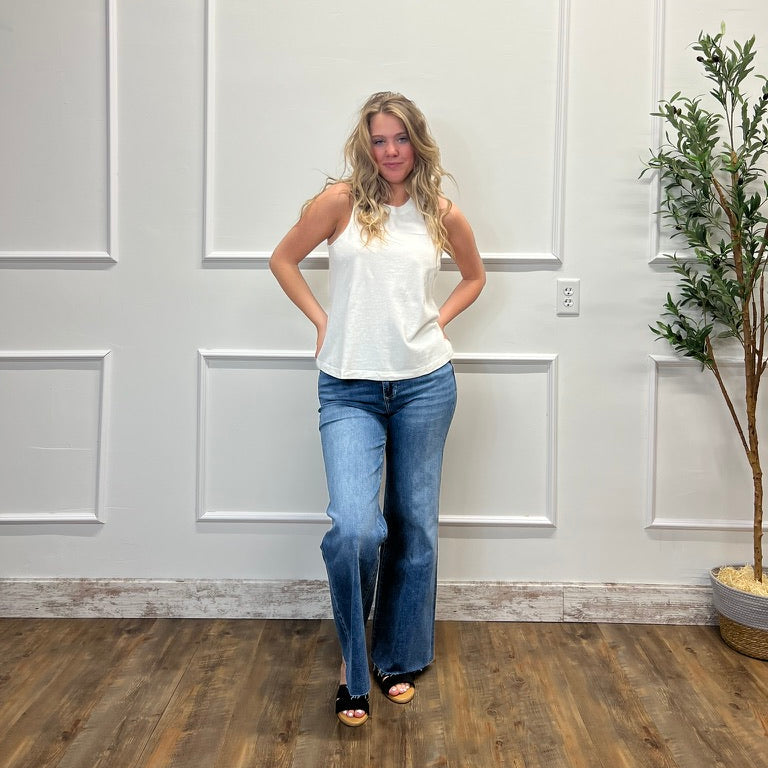 Woman in a white top and blue jeans standing in a room with white paneled walls and a plant.