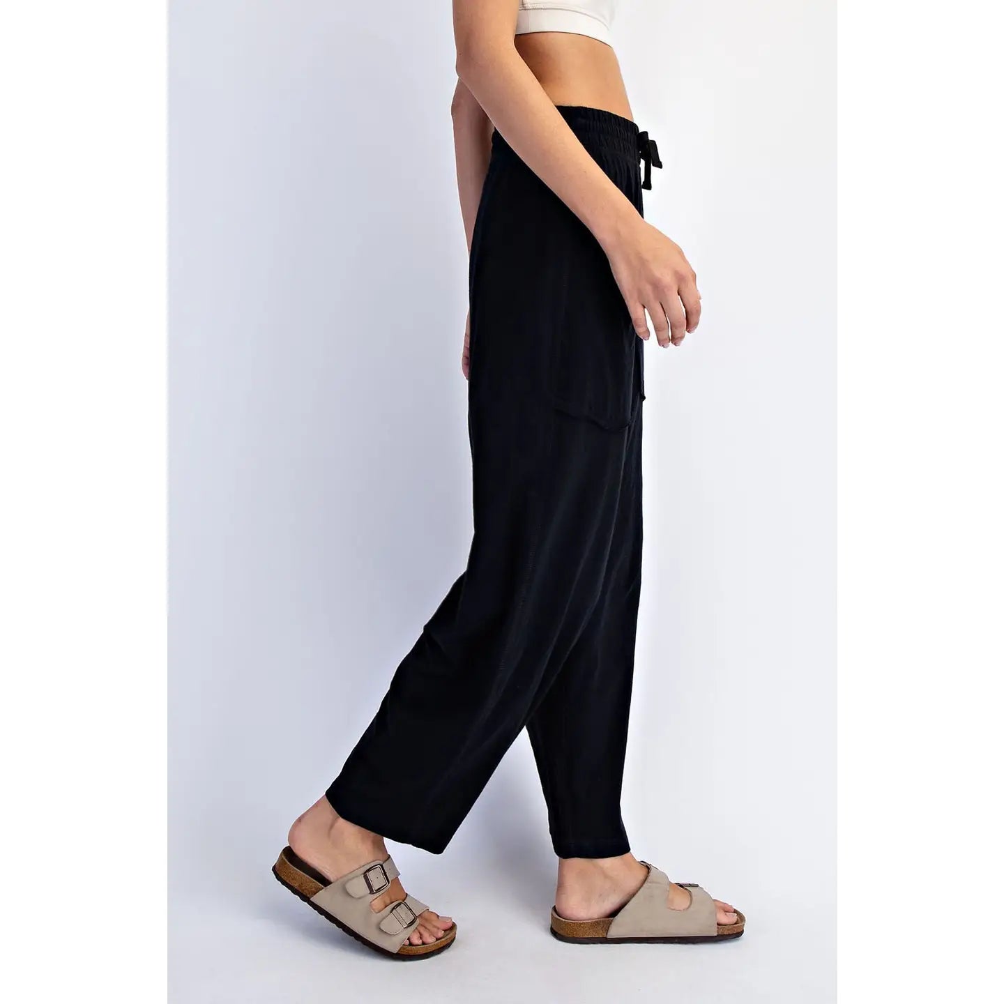 A model wearing black wide-leg drawstring pants and beige double-strap slide sandals, shown from the waist down against a light gray studio background.