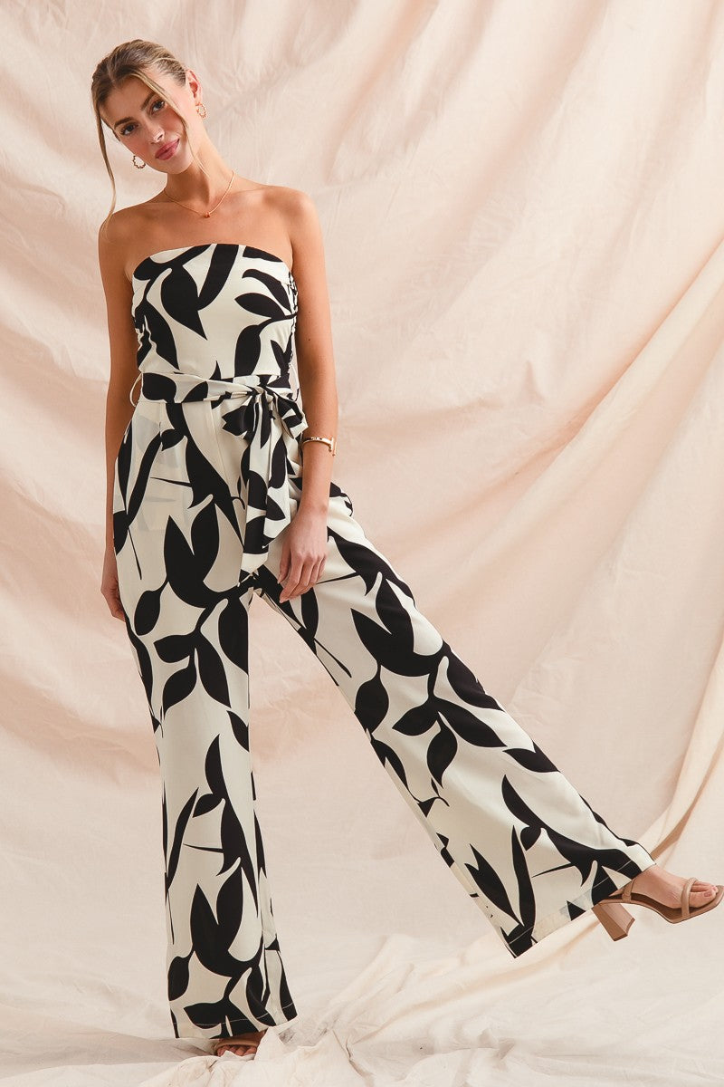 Woman wearing a strapless jumpsuit with black leaf pattern against a beige background
