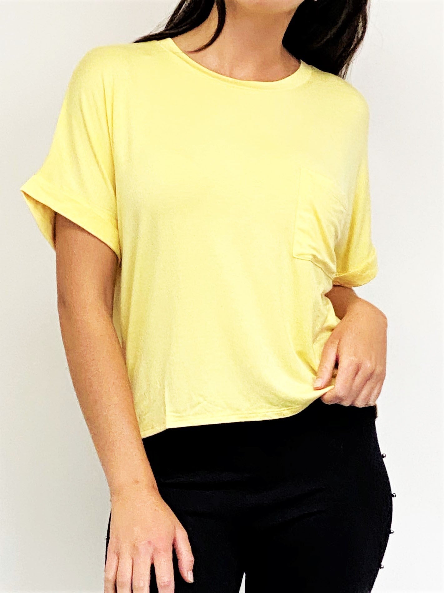 A woman wearing a pale yellow short-sleeve crewneck t-shirt and black pants, shown from the neck down against a plain white background.
