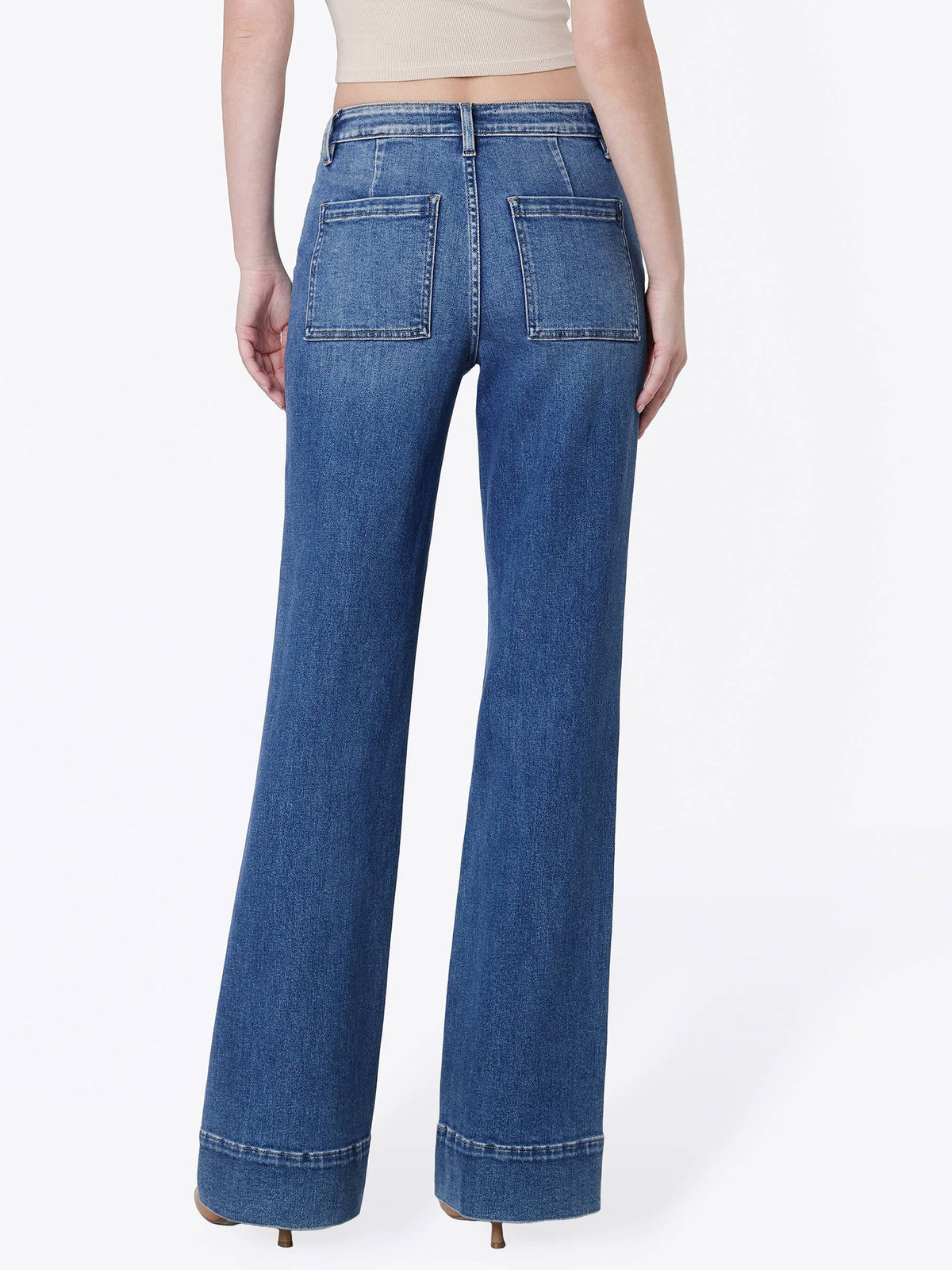 Rear view of a model wearing blue wide-leg jeans with a cuffed hem and back pocket details, paired with a beige crop top against a white studio background.