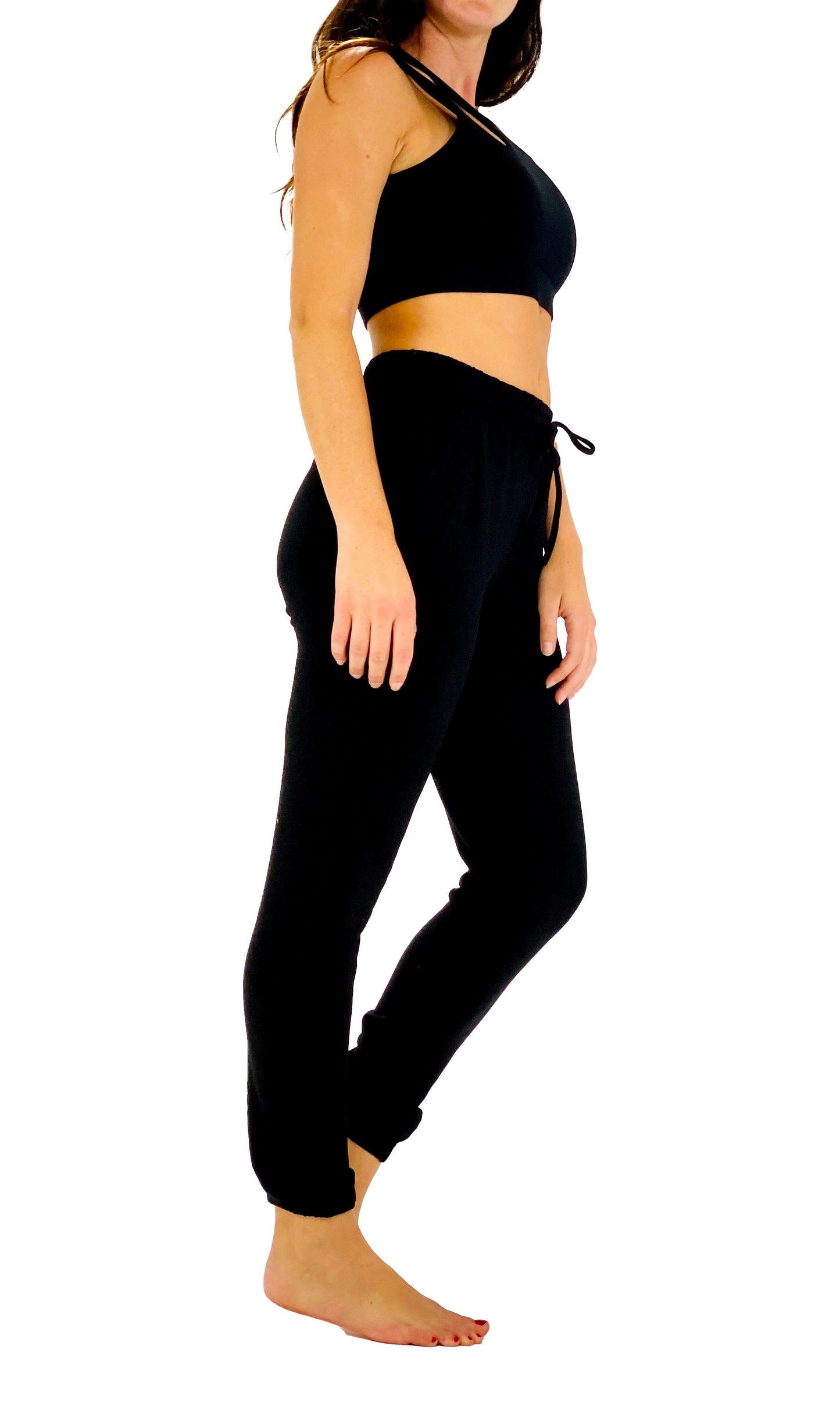 A woman modeling a black two-piece loungewear set consisting of a halter-style sports bra and matching drawstring jogger pants, shown against a plain white background.