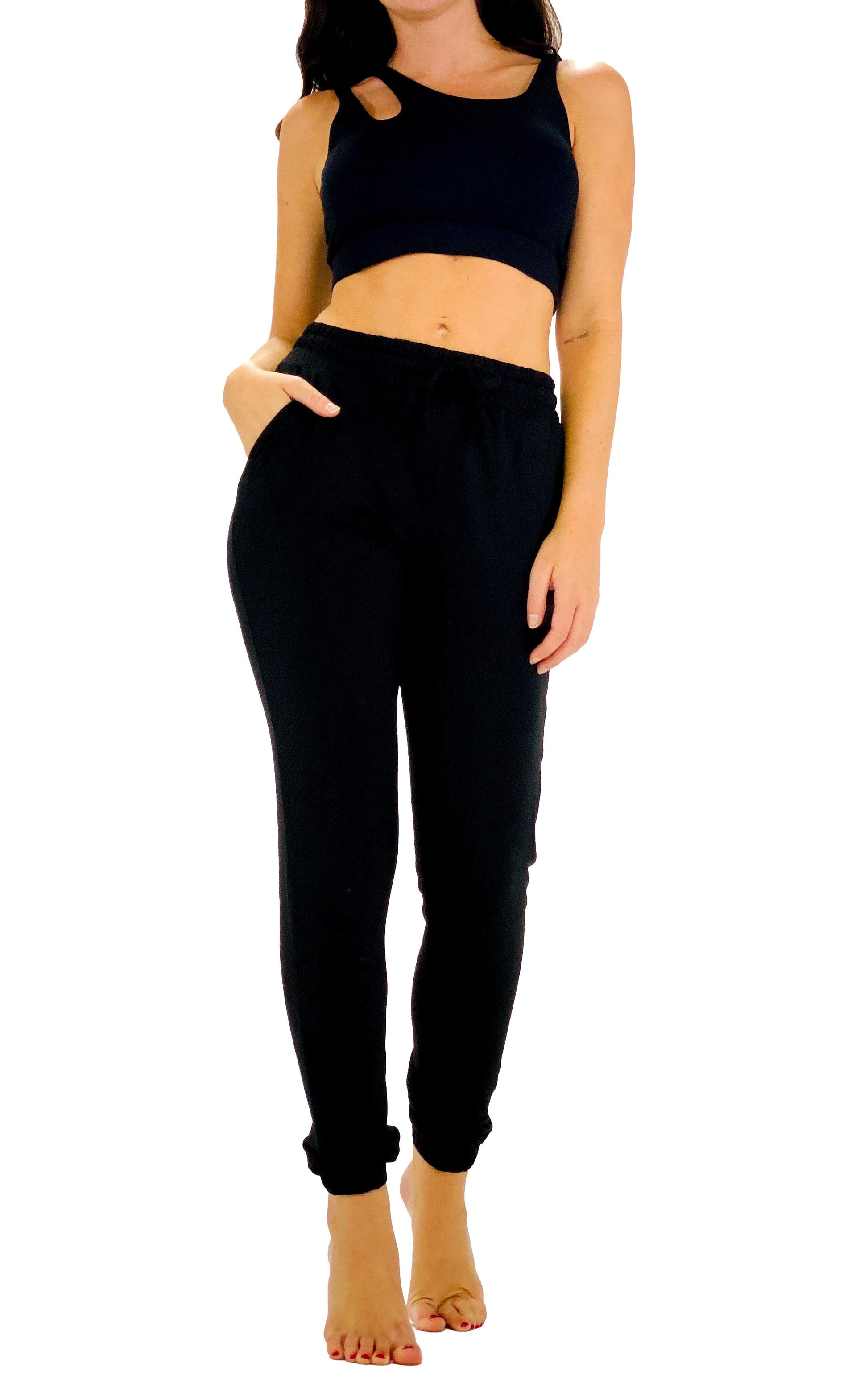 A woman modeling a black two-piece lounge set consisting of a cropped tank top with shoulder cutouts and matching jogger pants with side pockets, shown against a plain white background.