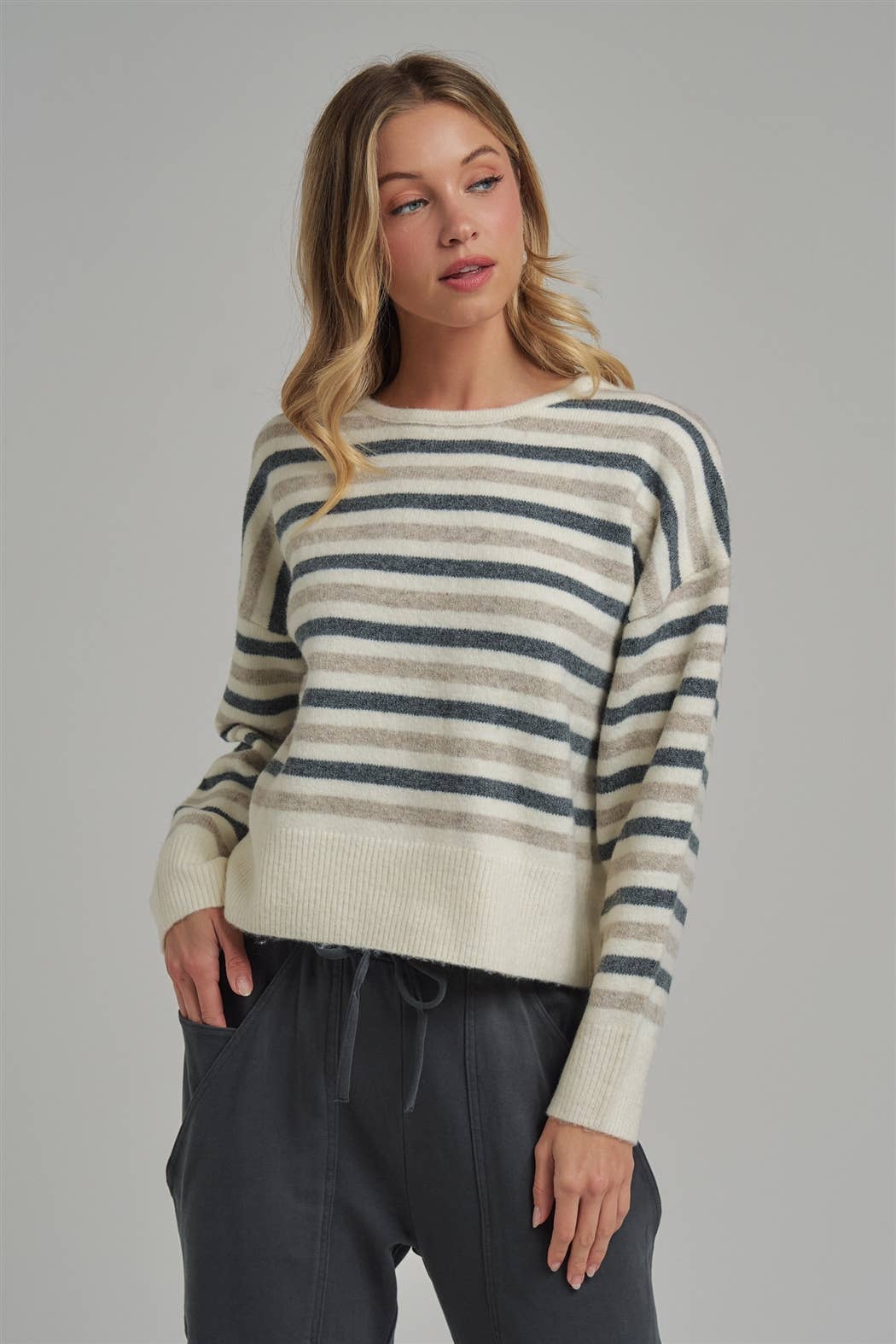 Woman wearing a striped sweater and dark pants against a plain background