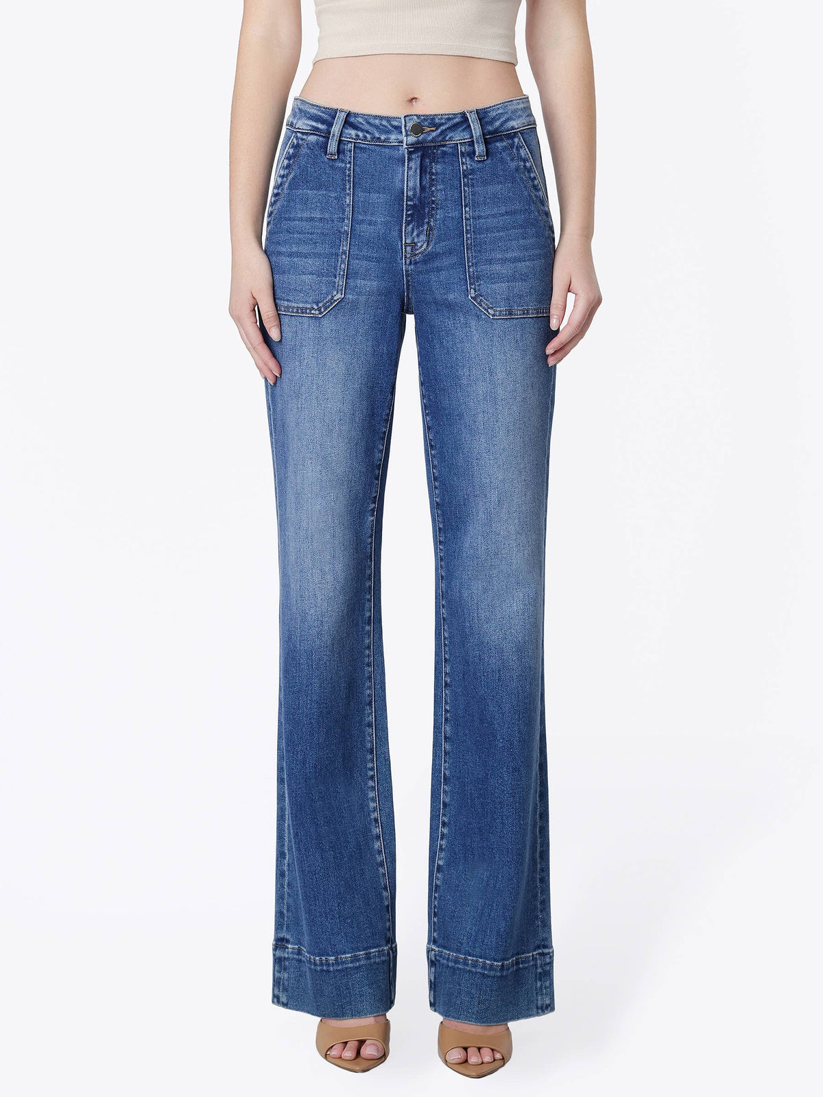 A model wearing a pair of medium-wash blue denim flare jeans with a high waist, styled with a beige crop top and brown sandals against a plain white studio background.