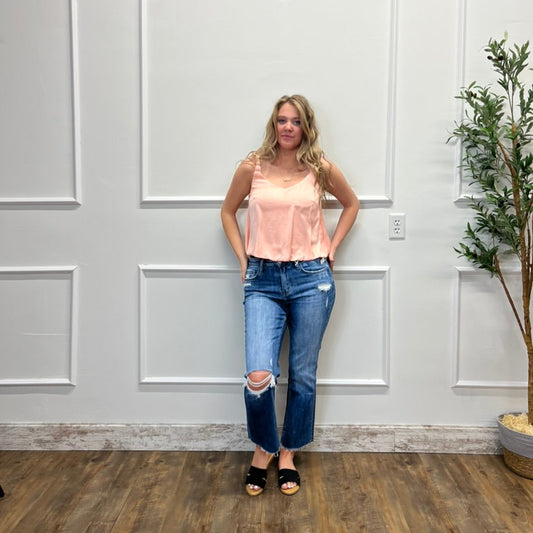 Woman in a pink top and blue jeans standing against a white paneled wall.