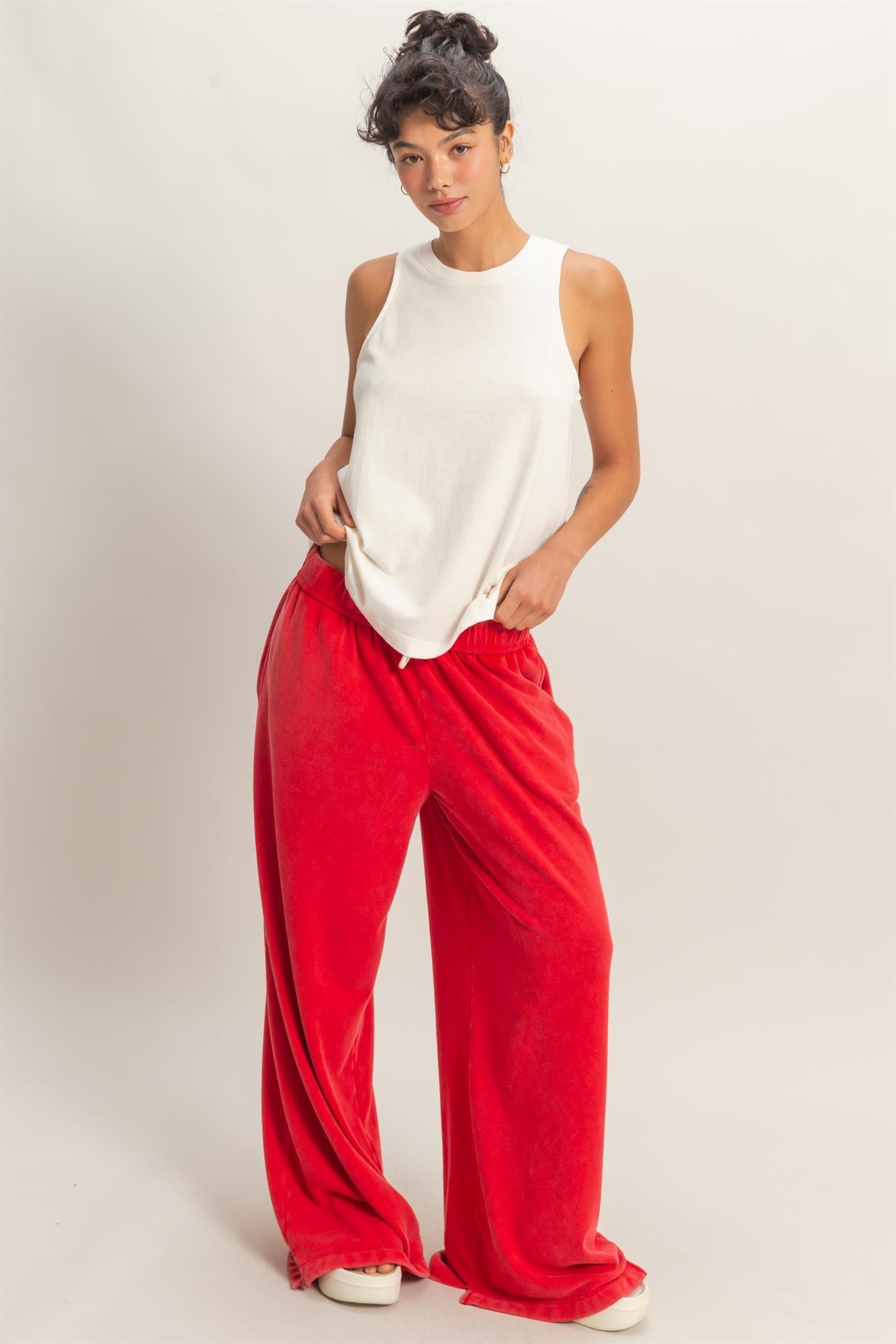 Woman wearing a white sleeveless top and red pants on a plain background