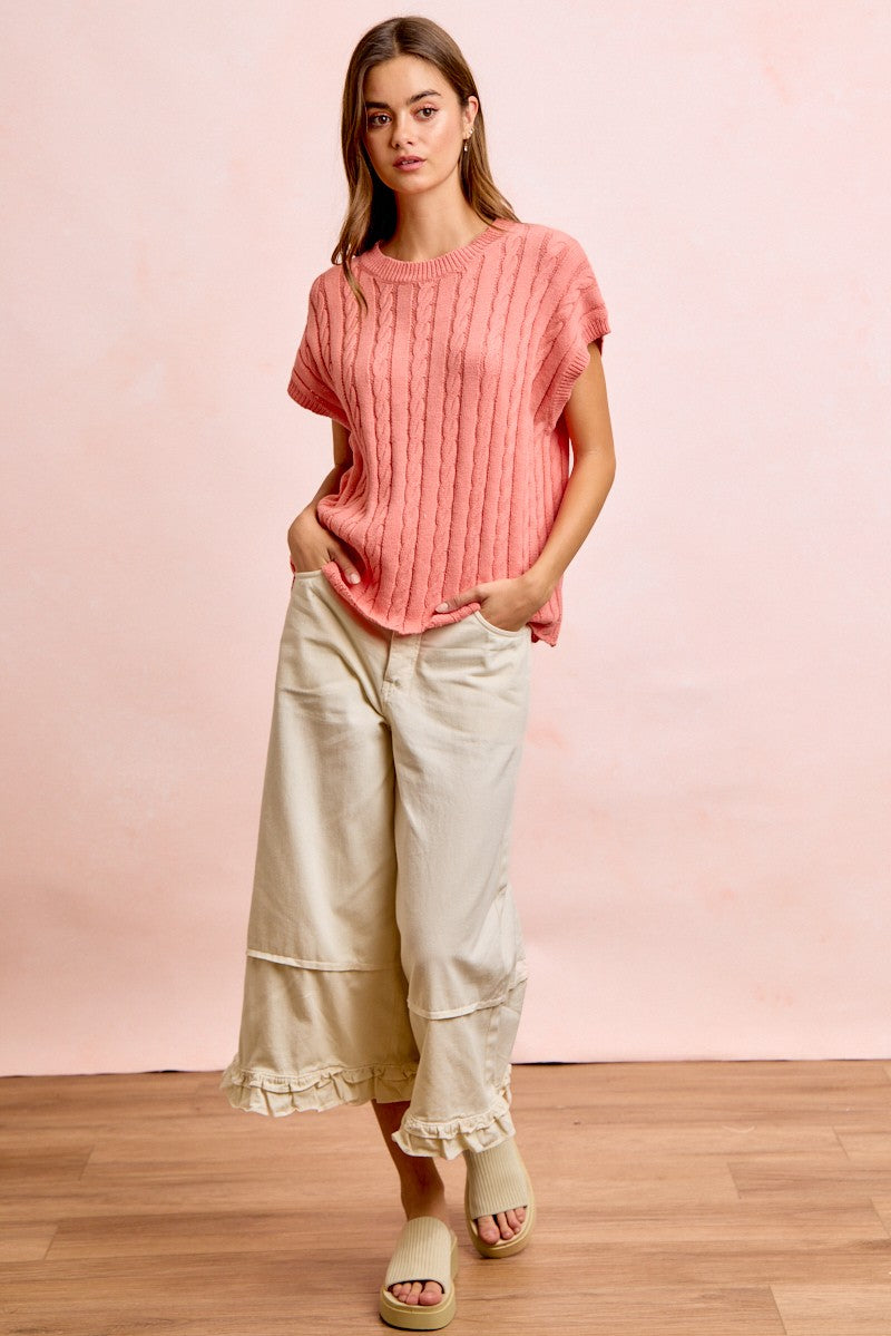 Woman wearing a pink ribbed top and beige wide-leg pants against a pink background
