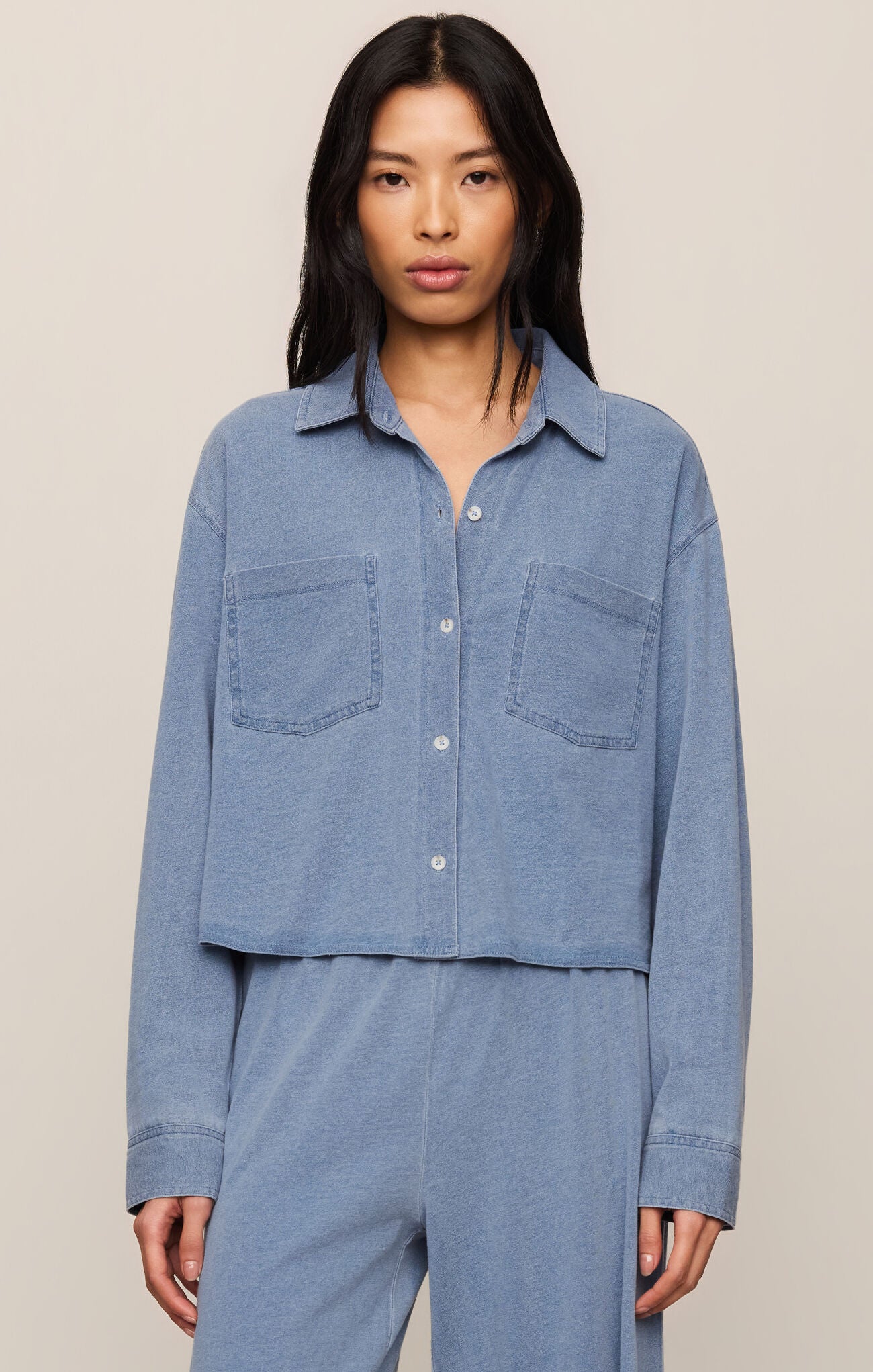 Woman wearing a blue denim shirt and pants on a beige background