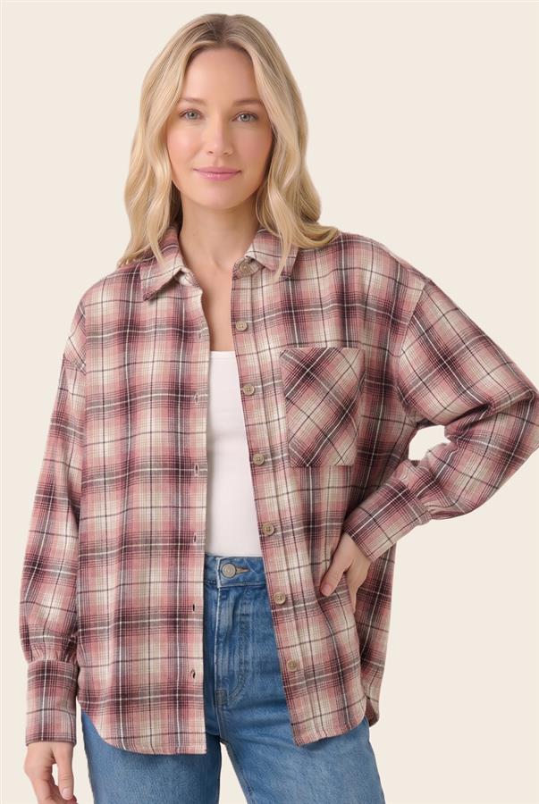 A woman wearing a long-sleeve button-up plaid flannel shirt in dusty pink, red, and beige tones, layered over a white tank top and blue jeans, against a solid light beige background.