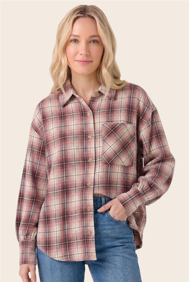 A woman wearing a long-sleeve button-up plaid shirt in dusty pink, brown, and cream, paired with blue jeans, against a solid light beige background.