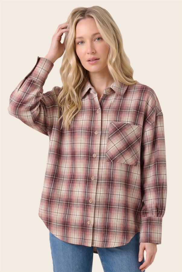 A woman modeling a long-sleeve button-up plaid shirt in muted pink, brown, and beige tones, paired with blue jeans against a solid light beige background.