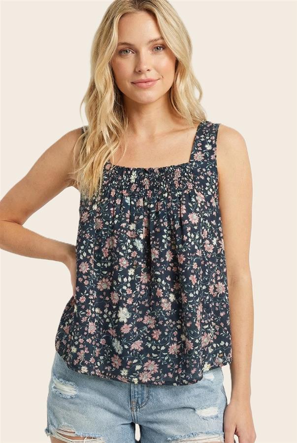 Woman wearing a floral sleeveless top and denim shorts on a beige background