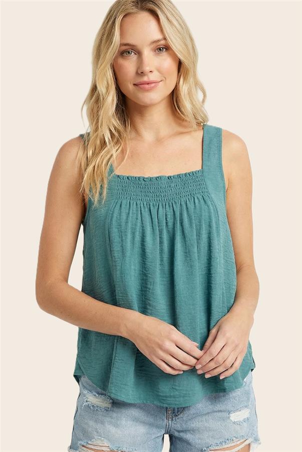 Woman wearing a teal sleeveless top and denim shorts on a beige background