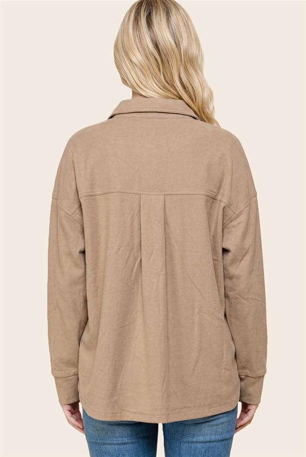 A woman viewed from the back wearing a loose-fit, long-sleeve utility-style jacket in a warm tan or camel color, paired with blue jeans, against a solid light beige background.