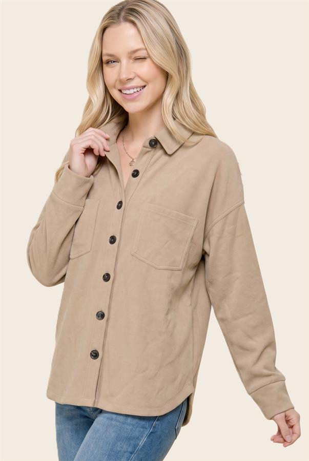 A woman wearing a beige long-sleeve button-up shirt with black buttons and a chest pocket, paired with blue jeans, against a solid light beige background.