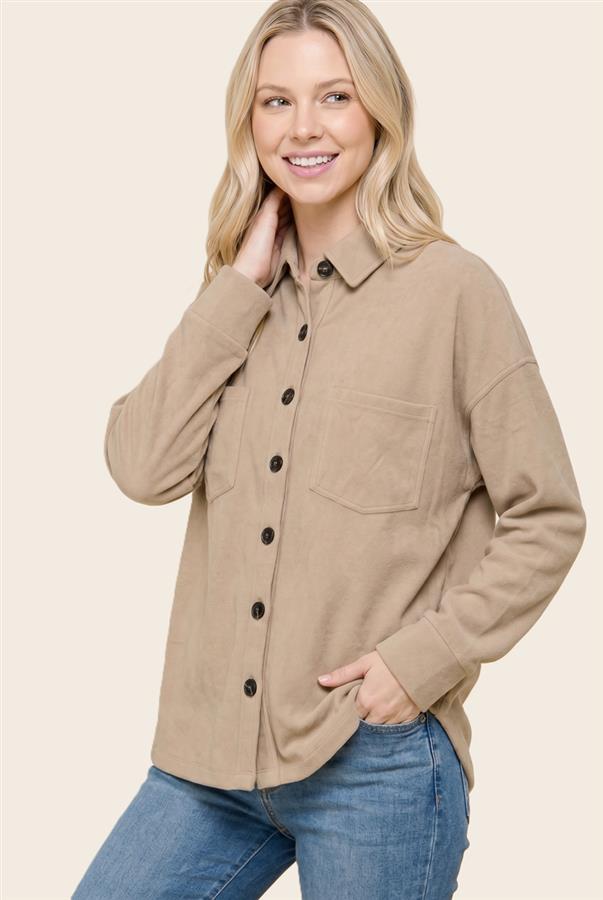 A woman wearing a relaxed-fit, long-sleeve button-up shirt in a warm tan/beige color, paired with blue jeans, against a solid light beige background.