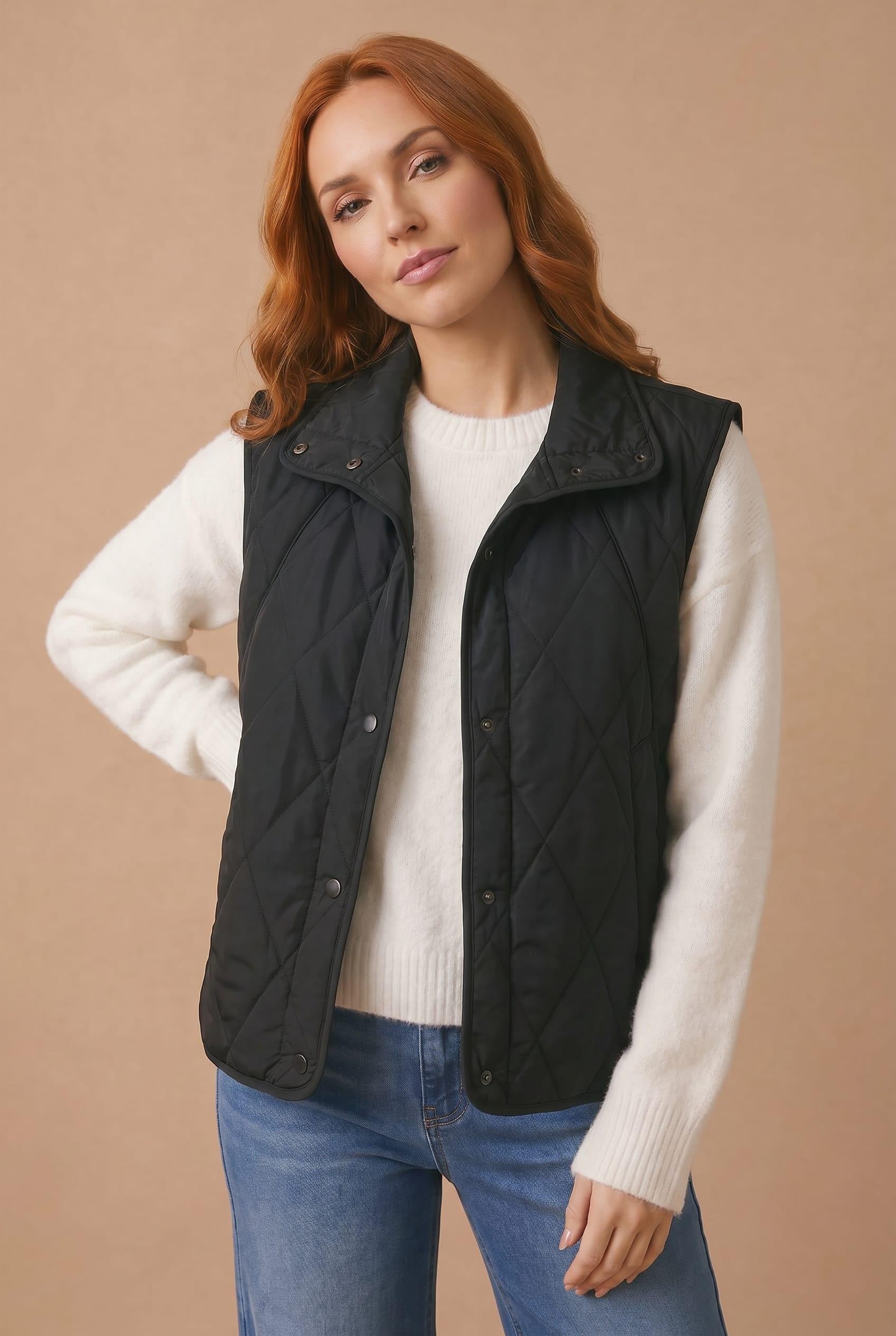 Woman wearing a black quilted vest over a white sweater on a beige background