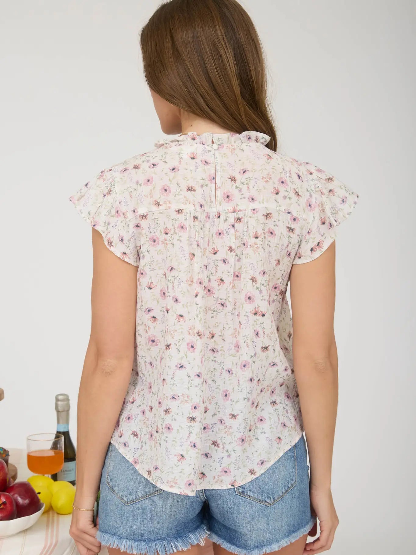 Woman wearing a floral blouse and denim shorts with a white background