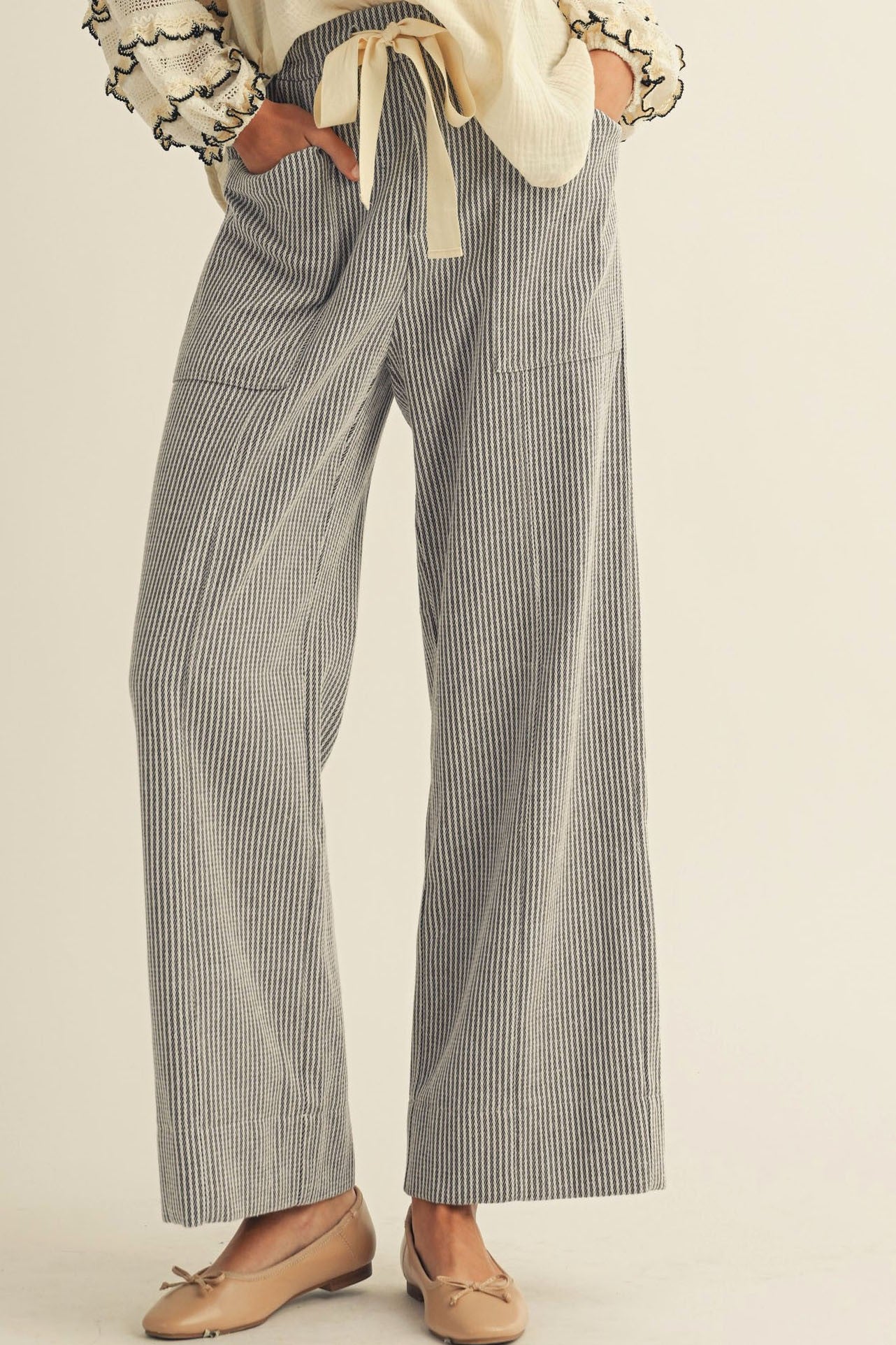Pinstripe pants worn with a cream top on a neutral background