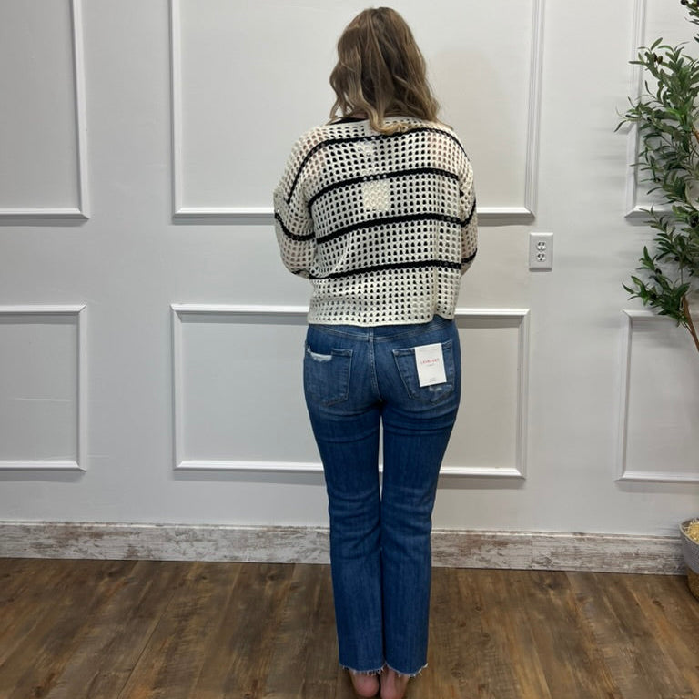 Person wearing a patterned sweater and blue jeans standing in a room with white paneled walls.