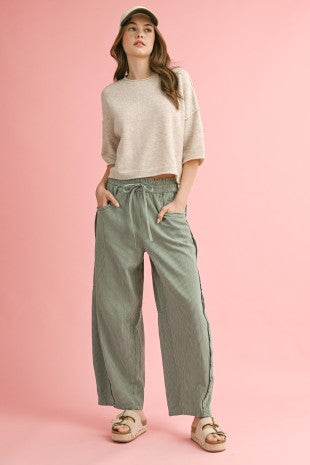 Woman wearing a light gray sweater and green pants on a pink background