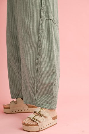 Person wearing green striped pants and beige sandals on a pink background