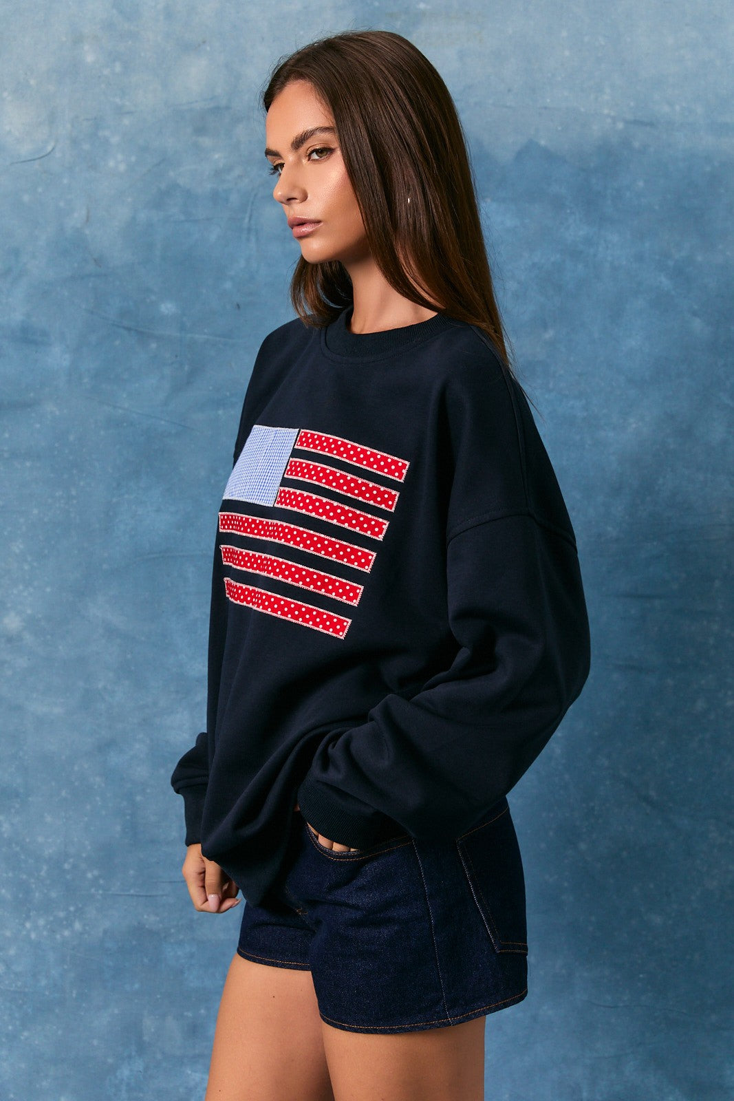 Woman wearing a black sweatshirt with a colorful graphic on a blue textured background