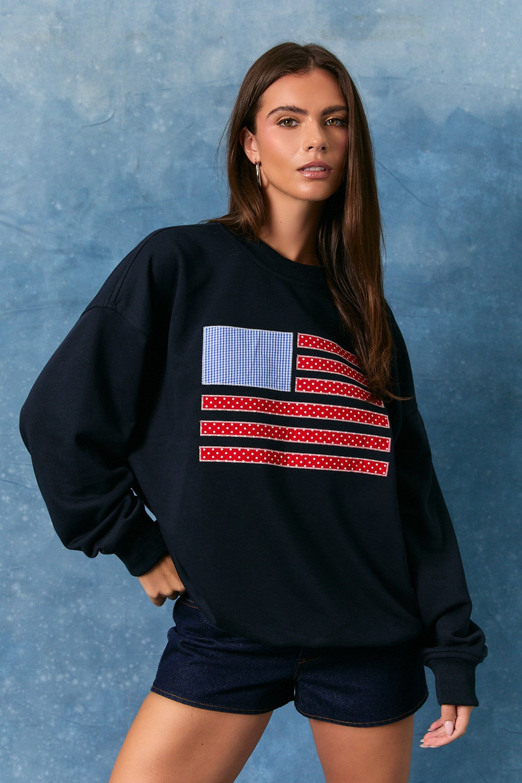 Woman wearing a black sweatshirt with an American flag design against a blue background