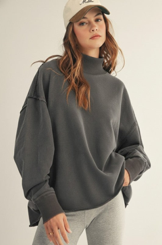 Woman wearing a gray oversized sweater and cap on a plain background