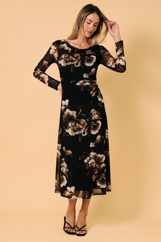 A woman modeling a black midi dress with a beige and brown floral pattern, featuring long sheer sleeves and a crew neckline, set against a solid beige background.