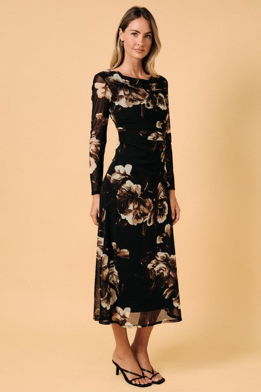 A woman modeling a long-sleeve midi dress with a black base and a large beige and brown floral print, set against a solid beige studio background.